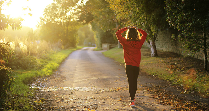 Natur und Sonnenaufgang. Person läuft mit dem Rücken zur Kamera weg und hält die Hände über dem Kopf